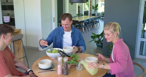 Smiling family sharing healthy salad and lemonade at modern open-plan kitchen table