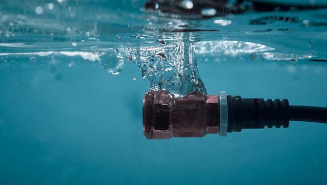 Waterproof metal connector splashing underwater, submerged cable junction, bubbles and ripples