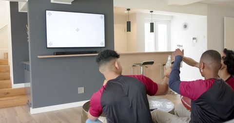 Friends watching game on blank tv, cheering with drinks and football in modern living room