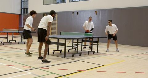 Group of Men Engaged in Competitive Table Tennis Match in Sports Hall