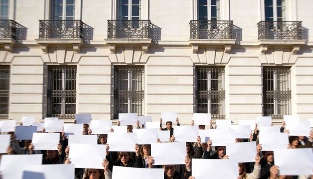 Large crowd holding blank placards outside neoclassical building protesting for change
