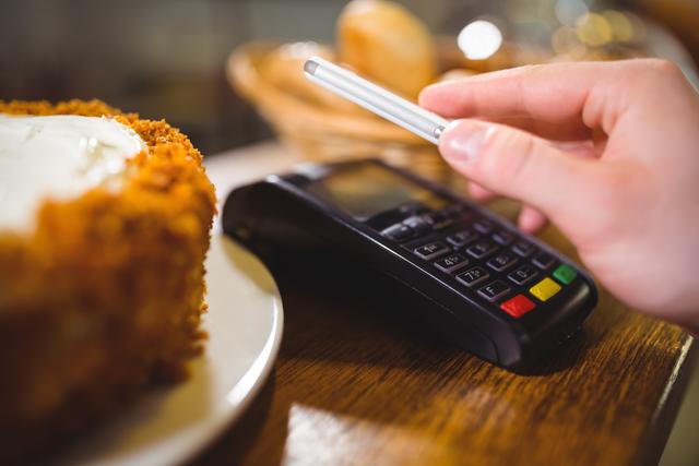 Customer using NFC technology for contactless payment in cafe. Ideal for articles or promotions about modern payment methods, technology integration in small businesses, and convenience in dining experiences.