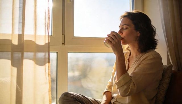 Woman sipping coffee on sunlit window seat embracing quiet morning calm cozy interior