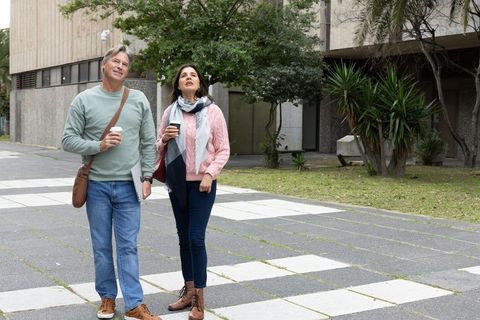 Middle-aged couple walking with takeaway coffee on urban campus plaza enjoying stroll