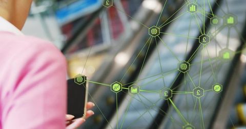 Holding smartphone in mall with green fintech network overlay, woman in pink blazer near escalator