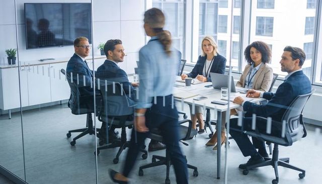 Executive team conducting strategic meeting around glass boardroom table with laptops
