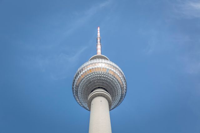 This image shows a low angle view of a TV tower ascending into a clear blue sky, highlighting its architectural design and importance as a communication and urban landmark. It can be used for educational materials, travel guides, architecture studies, promotional content about tourism or city landmarks, or as a modern, minimalistic background.
