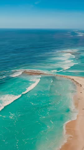 Vertical drone footage gliding over turquoise lagoon, sandbar and rolling coastline waves
