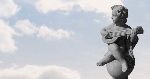 Stone Angelic Sculpture with Lute Against Cloudy Sky