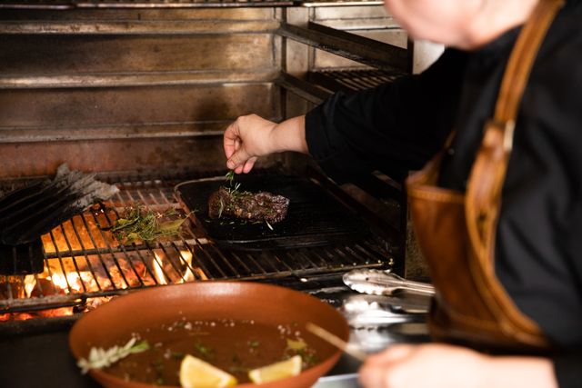 Side view close up of a Caucasian male chef working in a restaurant kitchen, putting fresh herbs on a grilled steak