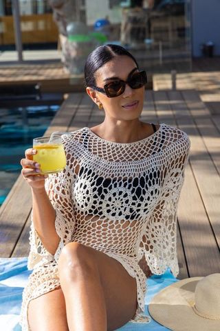 African american woman relaxing by pool in crochet coverup and black bikini sipping drink