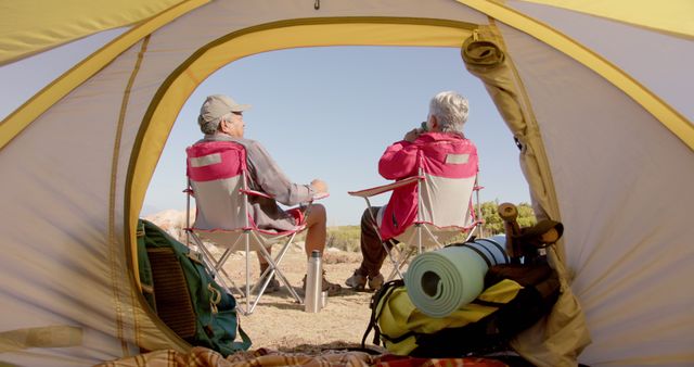 Back view of happy diverse senior couple sitting and talking on camping in mountains. Retirement, vacations, togetherness, summer, active senior lifestyle, unaltered.
