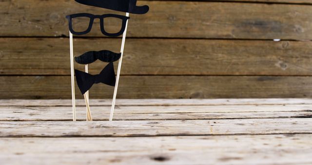 A pair of paper glasses and a mustache on sticks are set against a wooden background, with copy space. These props are often used in photo booths for fun and playful photography at parties or events.