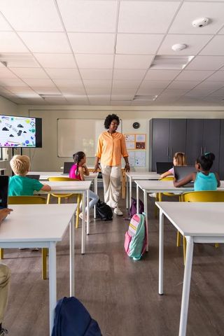 African American teacher leading primary class in bright classroom with colorful backpacks