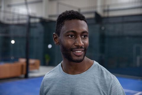 Smiling african-american man standing on indoor court wearing gray tee, friendly fitness