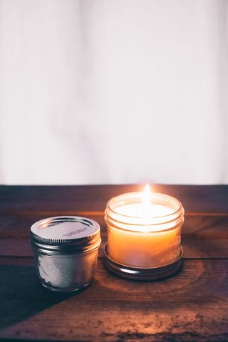 Lit Scented Candle Next to Closed Jar on Wooden Surface