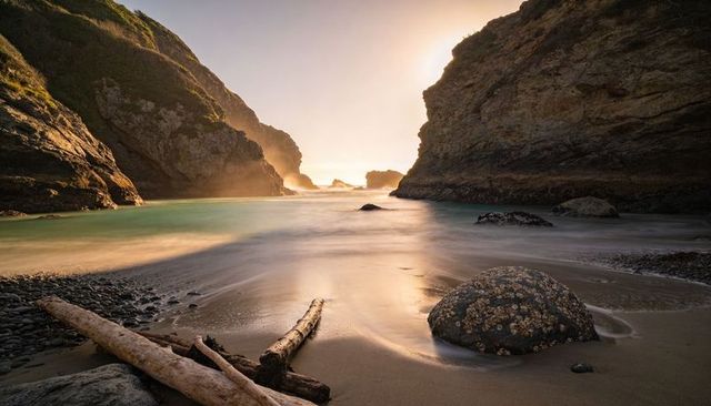 Secluded rocky cove bathing in golden hour light with driftwood and barnacled boulder