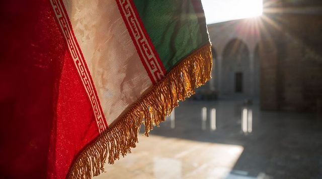 Sunlit tricolor flag with gold fringe and tassels hanging in historic courtyard arches