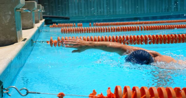 Competitive swimmer executing a powerful freestyle stroke in a well-maintained swimming pool with clear blue water. Ideal for use in promotions for swimming lessons, fitness campaigns, aquatic sports events, or training guides.