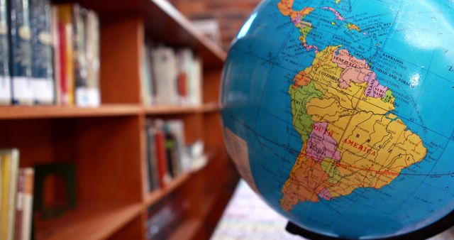 Picture highlighting a globe with South America prominently displayed in a library setting filled with bookshelves. Useful for educational purposes, academic articles, geography-related content, and materials promoting learning and knowledge acquisition.