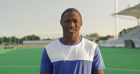 Smiling field hockey player on green pitch on sunny day