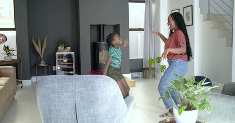 Mother and daughter dancing in sunlit modern living room with houseplants and fireplace