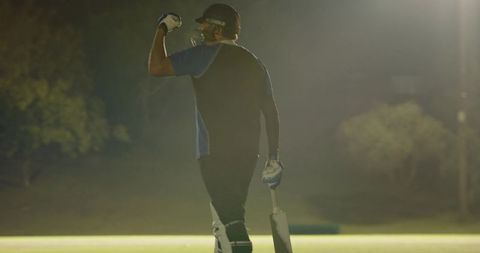 Night cricket batsman celebrating moment under floodlights holding bat and raising fist