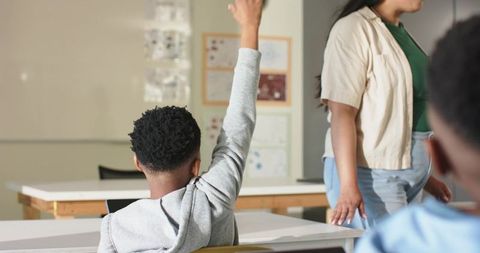 African american student raising hand while teacher walking between desks