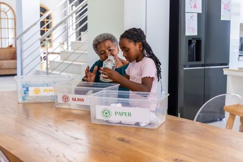 African american grandmother teaching granddaughter recycling at kitchen table