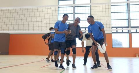 Diverse male volleyball team checking phone together after match in bright indoor gym