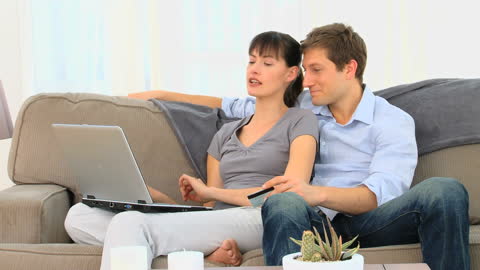 Smiling Couple Browsing Laptop Together on Comfortable Sofa