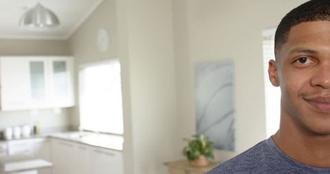 Young man standing and smiling in modern bright kitchen with left copy space