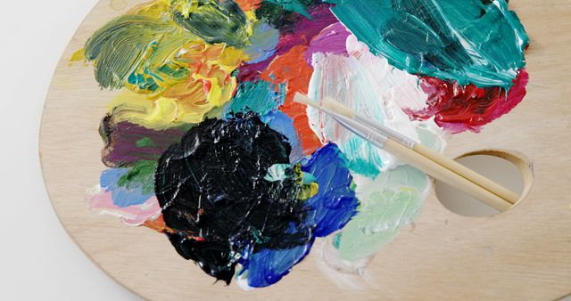Wooden palette displaying an array of vibrant paints mixed together with two brushes resting on it. Great for illustrating creativity, artistic activities, painting tutorials, DIY art projects, and educational content related to art.