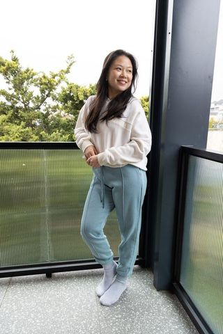 Asian woman standing on balcony in cozy loungewear smiling, relaxed urban morning