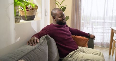 Mid-adult African American man smiling while relaxing on gray sofa in bright living room