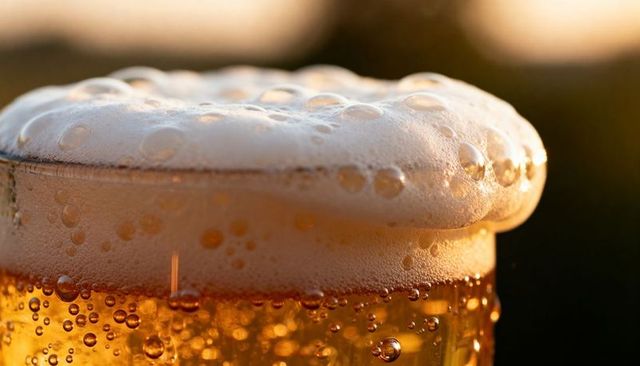 Glowing amber beer pint with frothy head and condensation droplets at golden hour