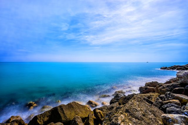 Vibrant coastal scene featuring clear blue waters meeting a rocky shoreline under a bright sky. Ideal for use in travel brochures, tourism advertisements, relaxation and wellness content, or nature-inspired blogs and websites.