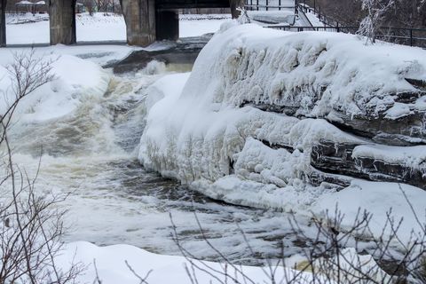 Icy river rapids flowing past snow-covered rock and concrete dam bridge, winter landscape