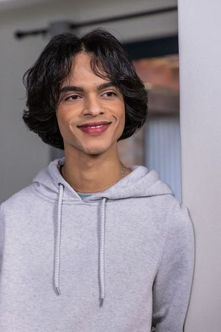 Indian teen smiling and leaning on pillar wearing gray hoodie and thin chain necklace