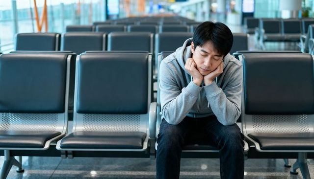 Tired asian traveler waiting at quiet airport gate resting head on hands on bench