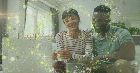 Happy St Patrick's Day Couple Relaxing on Couch with Laptop, Gold Confetti and Text Overlay