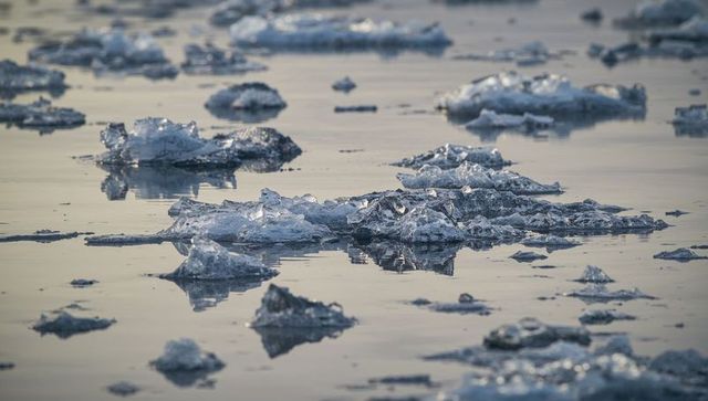 Drifting ice floes in glacial lagoon reflecting muted light, crystalline fragments floating