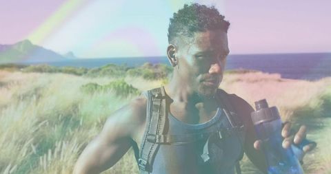 Hiker resting on coastal dune holding water bottle with ocean horizon, grasses, backpack