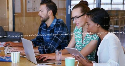 Collaborating team analyzing data on laptops and tablet in modern office workspace