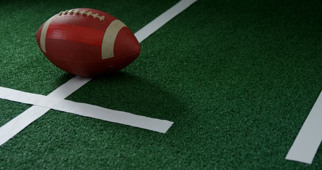 An American football rests on the green turf at a yard line, symbolizing a pause in the action of the game. Its position on the field suggests a focus on strategy and the next play in a football match.