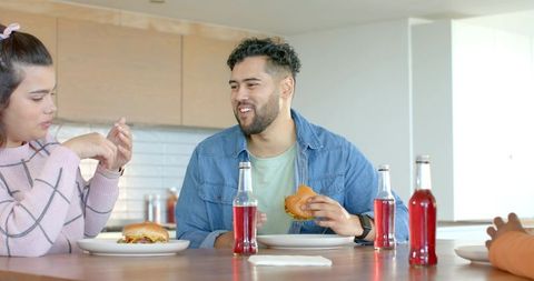 Friends enjoying burgers and soda at sunlit kitchen island during casual home gathering