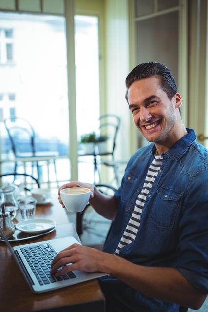 Portrait of smiling man using laptop while having coffee in cafÃ©