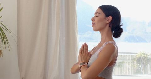Young Woman Practicing Meditation Indoors Near Large Window