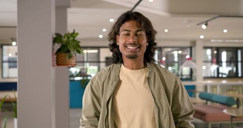 Smiling adult african american man standing in coworking lounge wearing olive jacket