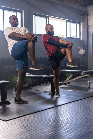 African men doing knee-to-chest balance stretch in gym training for mobility